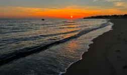 Bright orange sunset over dark blue ocean waves. There are a few wispy clouds in the sky.