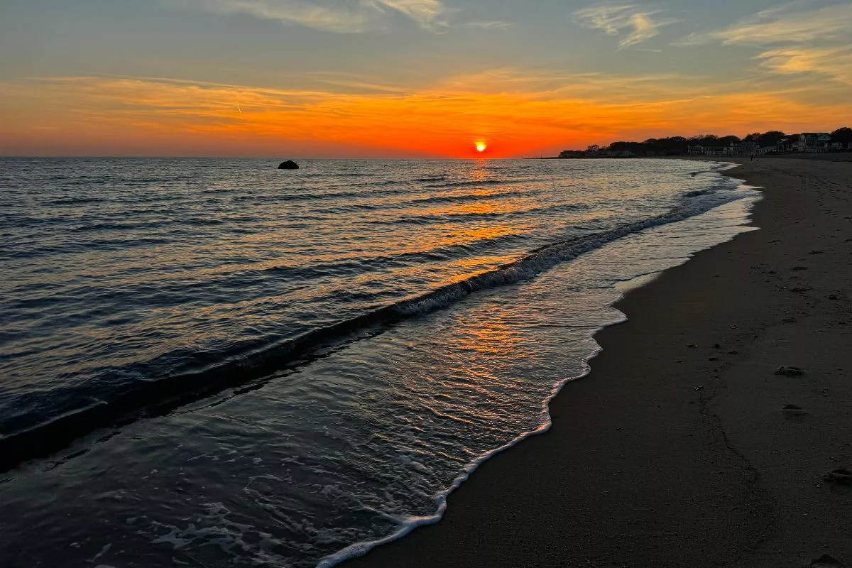 Bright orange sunset over dark blue ocean waves. There are a few wispy clouds in the sky.