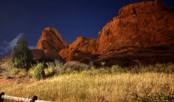 Red Rocks under a night sky with a few stars. A wooden fence in the foreground.