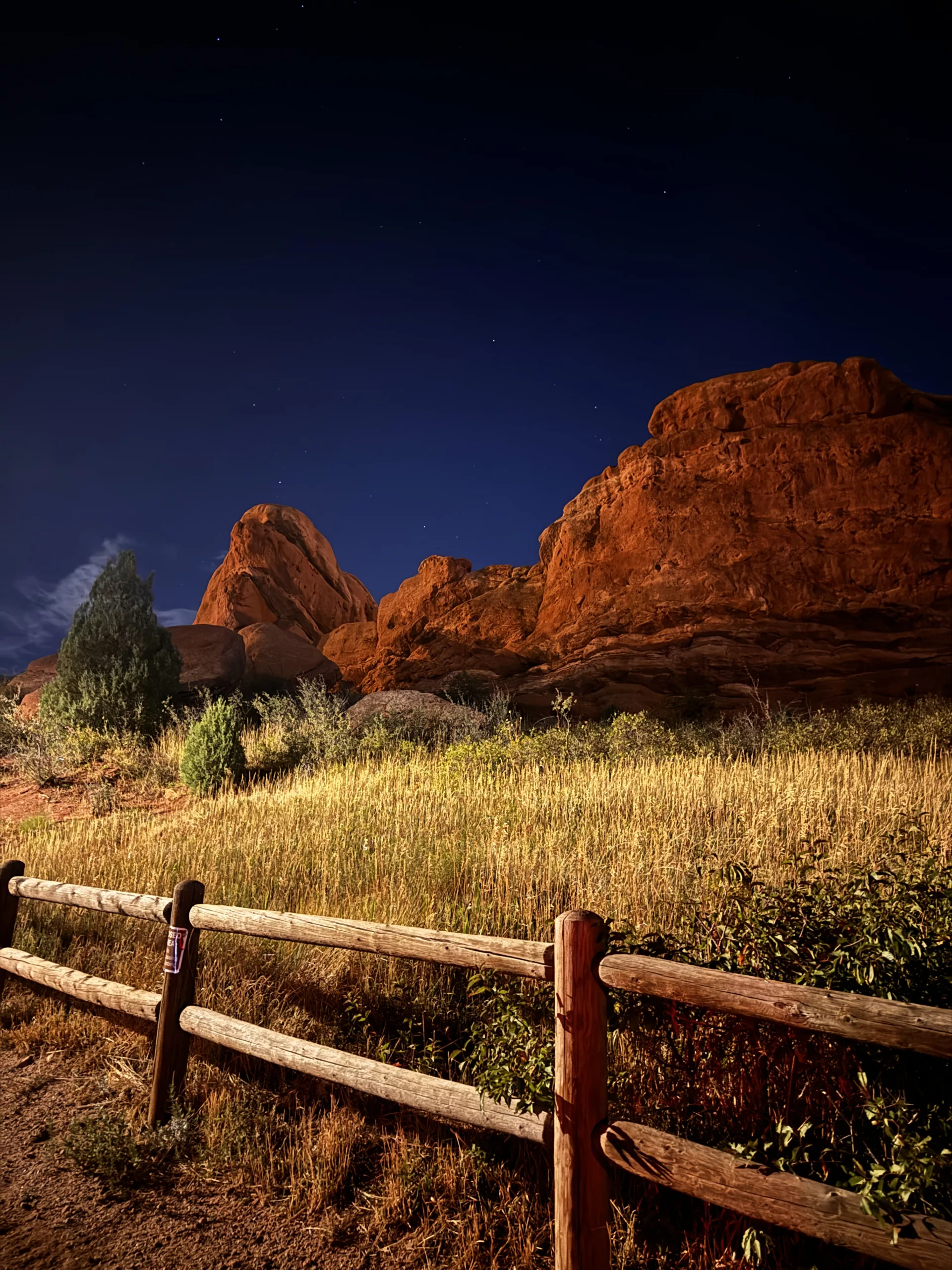 Red Rocks under a night sky with a few stars. A wooden fence in the foreground.